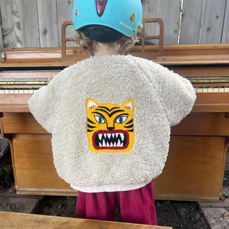 Child wearing a fluffy white jacket with a tiger design, standing outdoors.
