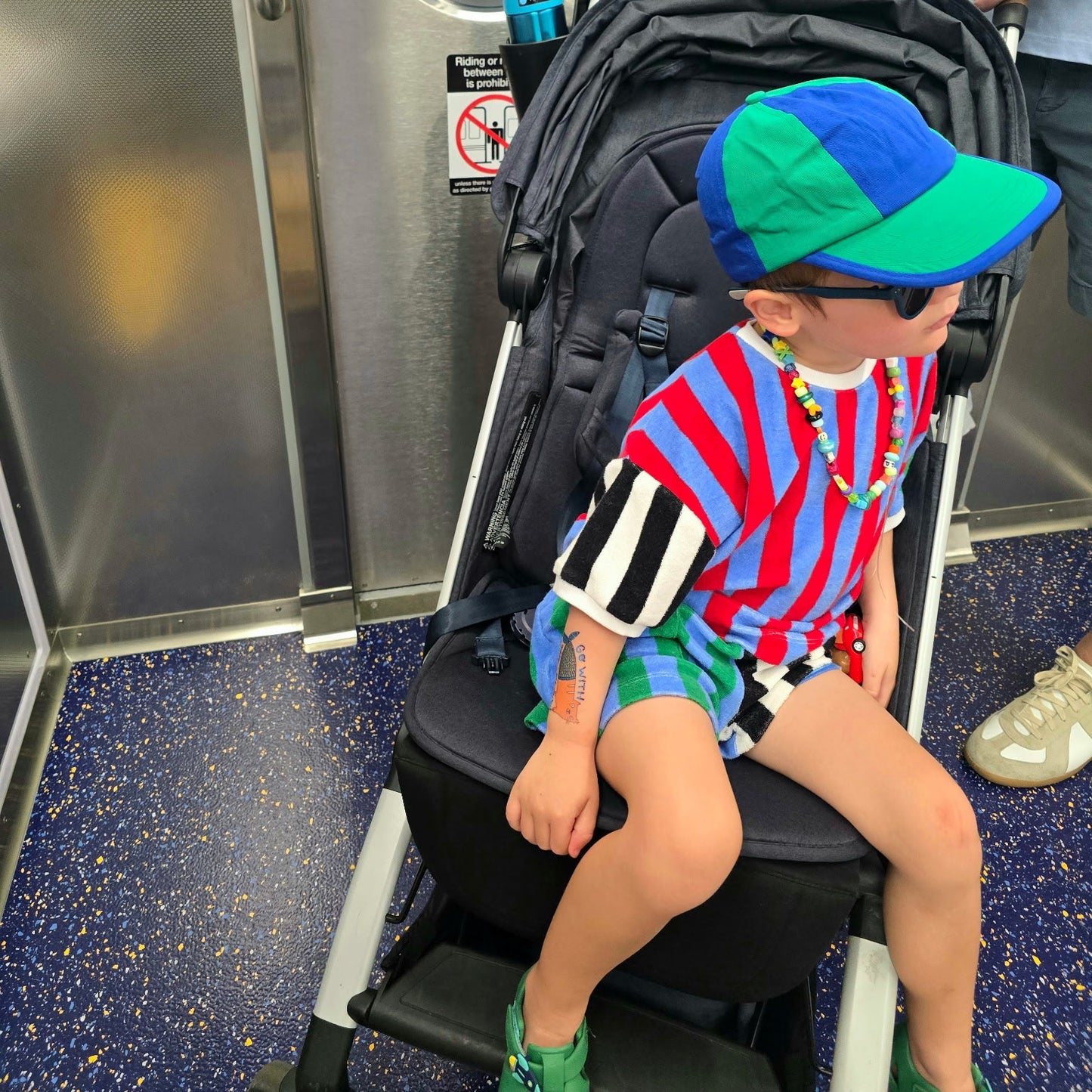 Child sitting on a stroller with a backpack in a subway car