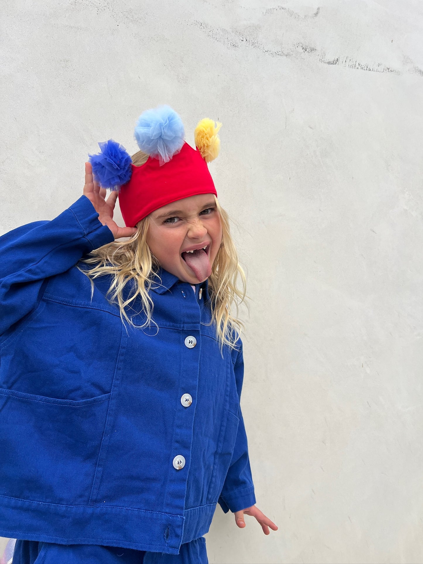 Child wearing a colorful hat with pom-poms and a blue coat against a light background