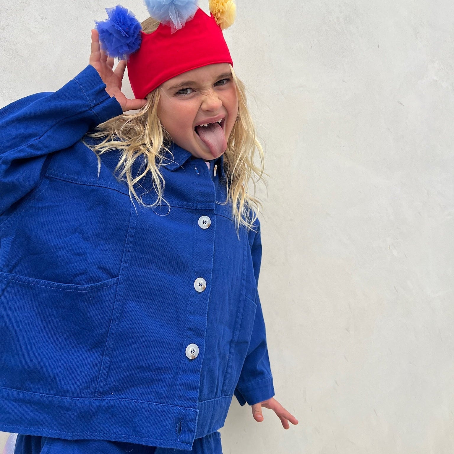 Child wearing a colorful hat with pom-poms and a blue coat against a light background