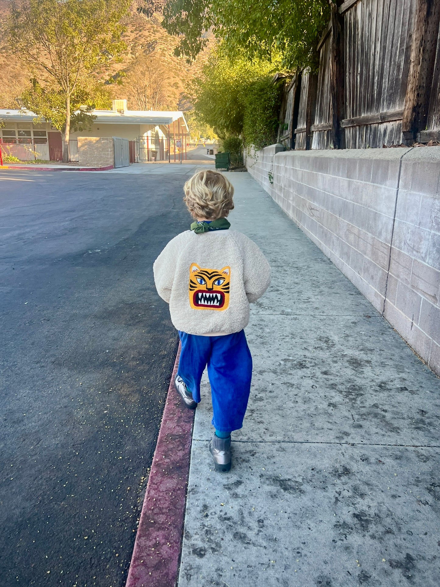 Child walking on a sidewalk with a building and trees in the background