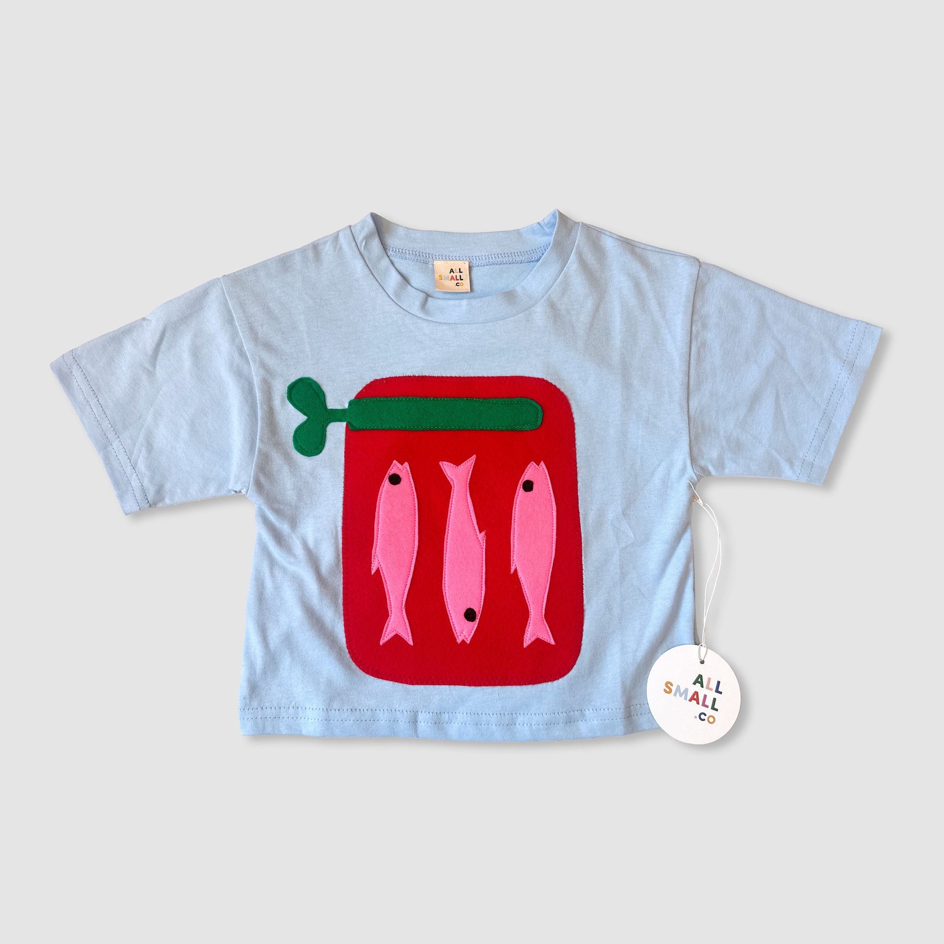 A blue children's t-shirt with a red pocket embellished with a sardine design and the brand tag showing 'Whimsy Ranch'.