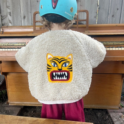 Child wearing a fluffy white jacket with a tiger design, standing outdoors.
