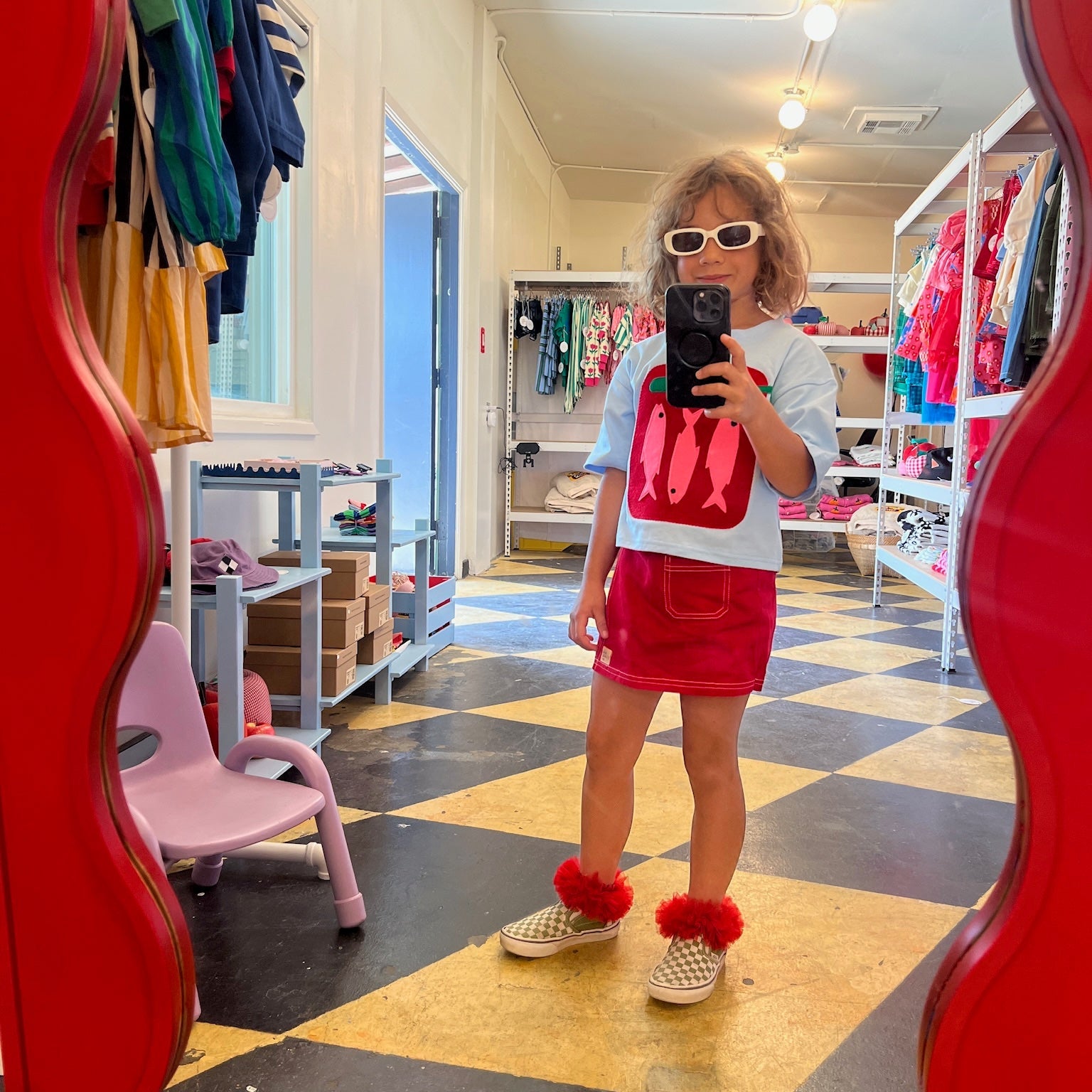 Child taking a mirror selfie in a store with colorful clothing and furniture.