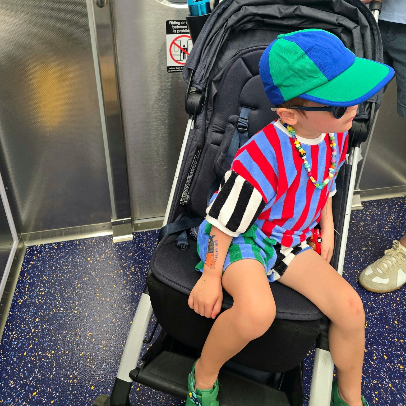 Child sitting on a stroller with a backpack in a subway car